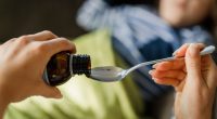 Close-up of a hand pouring medicine into a spoon for a child.
