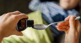 Close-up of a hand pouring medicine into a spoon for a child.