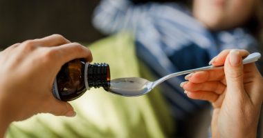Close-up of a hand pouring medicine into a spoon for a child.