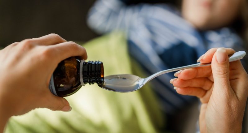 Close-up of a hand pouring medicine into a spoon for a child.