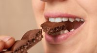 Close-up of a woman biting a piece of chocolate.