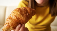 Teenage girl eating croissant for breakfast, close up