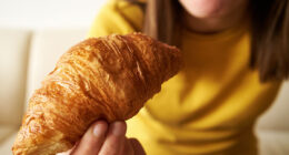 Teenage girl eating croissant for breakfast, close up