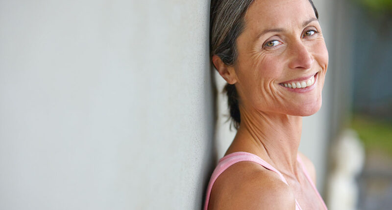 Happiness is an inside job. Portrait of an attractive mature woman in gymwear leaning against a gray wall.