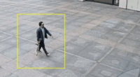 Man walking on a plaza carrying a long object.