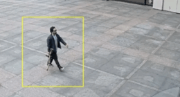 Man walking on a plaza carrying a long object.