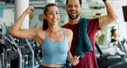 Happy athletic couple flexing their muscles after working out in a gym and looking at camera.