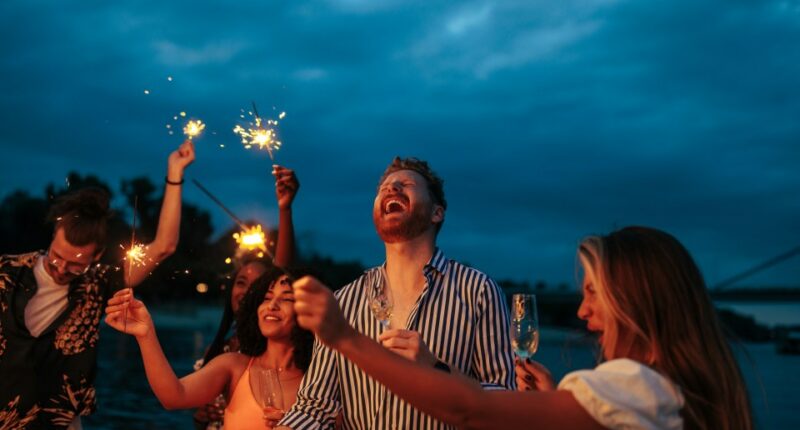 Group of friends celebrating with sparklers and drinks at night.