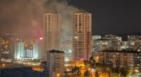 Nighttime view of a city with smoke rising from a building fire.