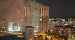 Nighttime view of a city with smoke rising from a building fire.