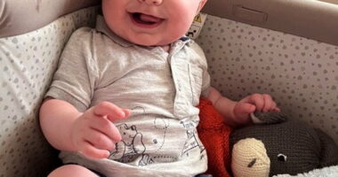Six-month-old baby sitting in a crib, smiling.