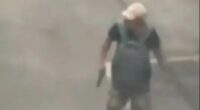 Surveillance footage of a man carrying a gun in a parking lot.