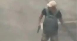 Surveillance footage of a man carrying a gun in a parking lot.
