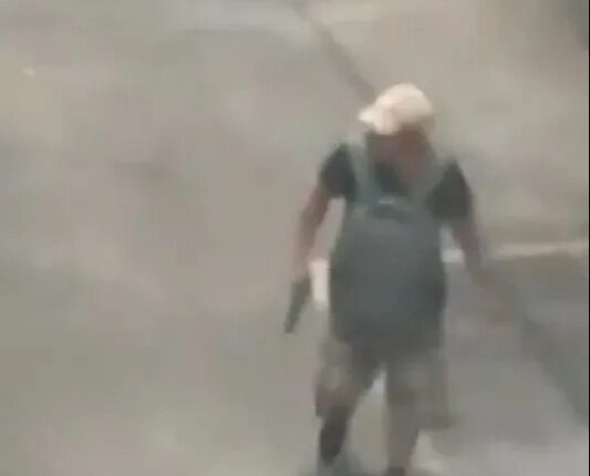 Surveillance footage of a man carrying a gun in a parking lot.