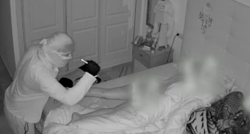 Security camera footage of a burglar looking at a sleeping woman.