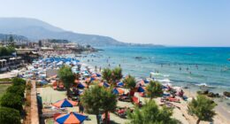 Beach scene with many people swimming and sunbathing under umbrellas.
