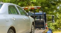 A silver car being towed on a flatbed tow truck.