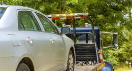 A silver car being towed on a flatbed tow truck.