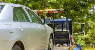 A silver car being towed on a flatbed tow truck.