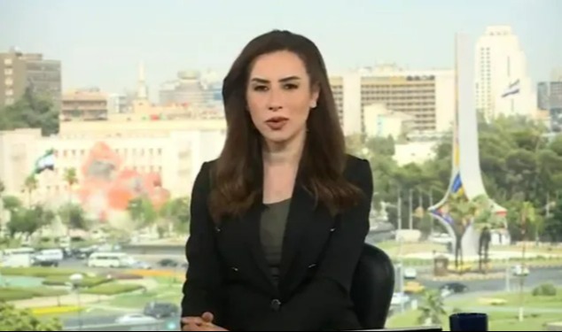 News anchor sitting in front of a window overlooking a city.