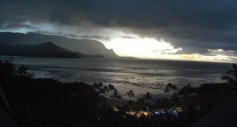 Ocean view at sunset with dark clouds and mountains in the background.