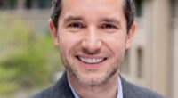 Portrait of a smiling man in a gray blazer.
