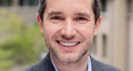 Portrait of a smiling man in a gray blazer.
