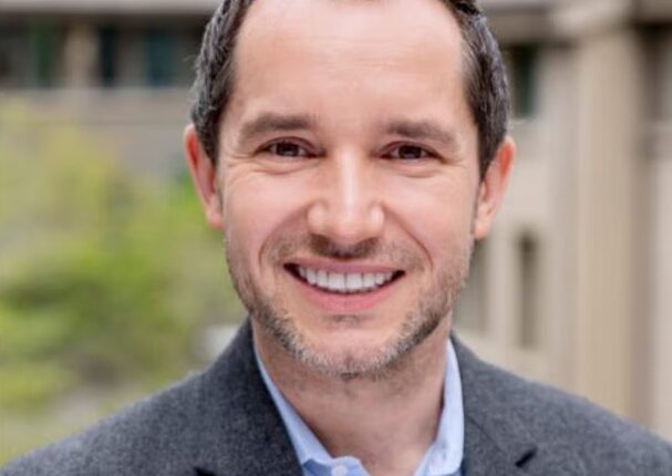 Portrait of a smiling man in a gray blazer.