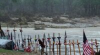 A makeshift memorial with crosses and flags for flood victims during a rainstorm.