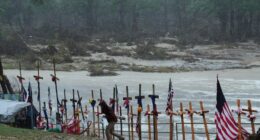 A makeshift memorial with crosses and flags for flood victims during a rainstorm.