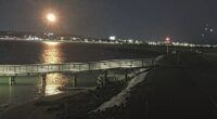 Nighttime view of a pier extending into a body of water with a city skyline in the background.