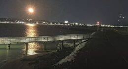 Nighttime view of a pier extending into a body of water with a city skyline in the background.