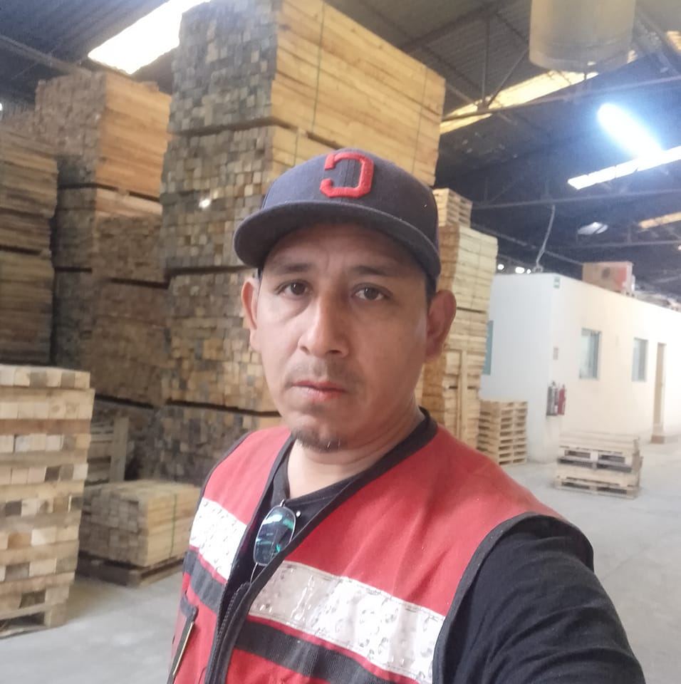 Man in a red safety vest standing in a lumberyard.