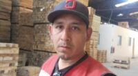 Man in a red safety vest standing in a lumberyard.