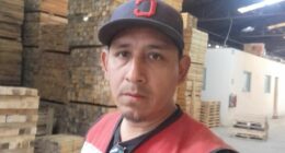 Man in a red safety vest standing in a lumberyard.