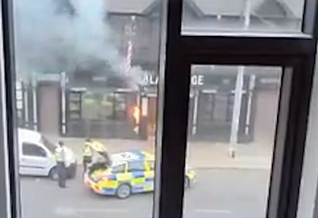 View from a window of a street scene with a small fire, police officers, and police cars.