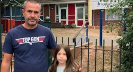 A girl and her father stand near floral tributes outside a school.