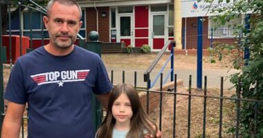 A girl and her father stand near floral tributes outside a school.