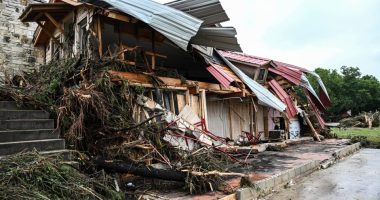 Flood-damaged home with roof torn off and debris scattered around.
