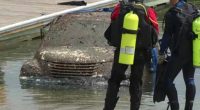 Mud-covered car pulled from water; divers nearby.