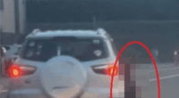 A blurred image of a person standing near the back of a car.