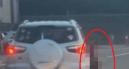 A blurred image of a person standing near the back of a car.
