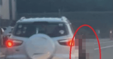 A blurred image of a person standing near the back of a car.