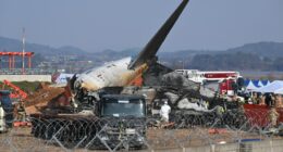 Burned wreckage of a plane at an airport with emergency personnel on the scene.