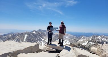 Two hikers on the summit of Mount Whitney holding a sign.