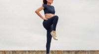 Sporty woman stretching leg muscles with standing single knee to chest stretch, knee drive