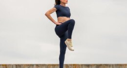 Sporty woman stretching leg muscles with standing single knee to chest stretch, knee drive