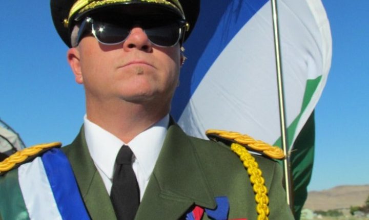 A man in a military uniform stands with a flag.