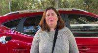 Woman being interviewed in front of a red car.
