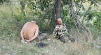 Two bound men sitting under a tree.